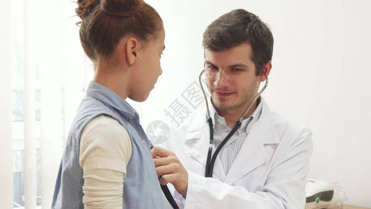 一个小女孩来看医生她站在治疗师旁边医生仔细聆听她的肺部为此图片