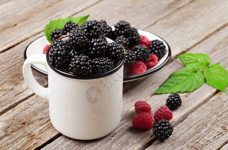 木桌上的一杯成熟的黑莓和覆盆子图片