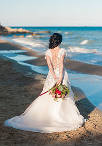 美丽的新娘穿着豪华婚纱与海边的花束海边的婚礼新娘在婚礼地点附近的海中图片