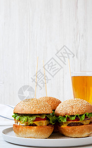 奶酪汉堡在灰色盘子和啤酒杯上白色木质背景侧图片