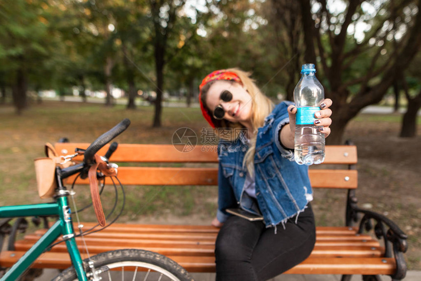 快乐时尚的女孩坐在自行车附近公园的长椅上图片