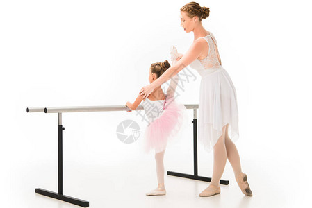 穿着芭蕾舞短裙的女教师帮助小芭蕾舞演员在白色背景中隔离的芭蕾舞台上图片