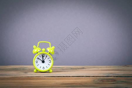木制桌和灰色背景上的绿色提醒时钟时间概图片