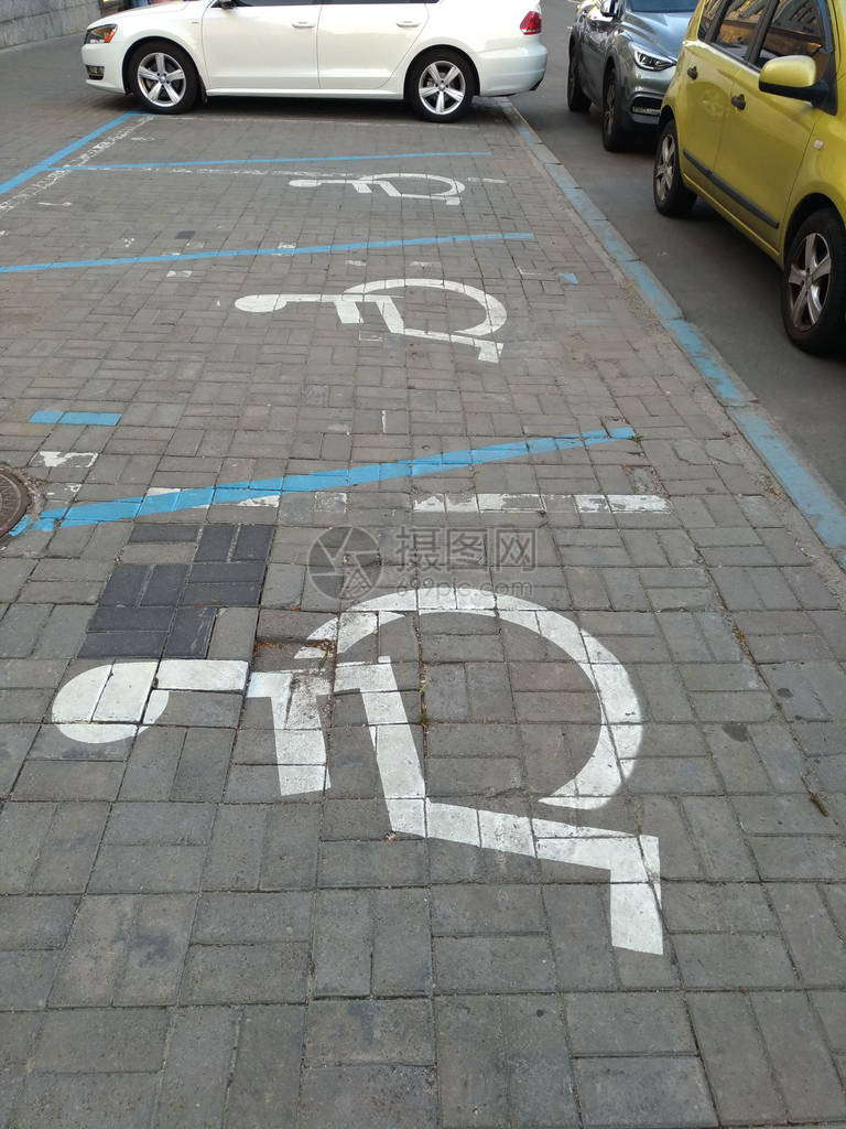 在汽车自然光轮椅符号之间的几个地方的瓷砖街道上为残疾人提供图片