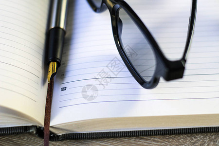 钢笔和眼镜放在笔记本上图片