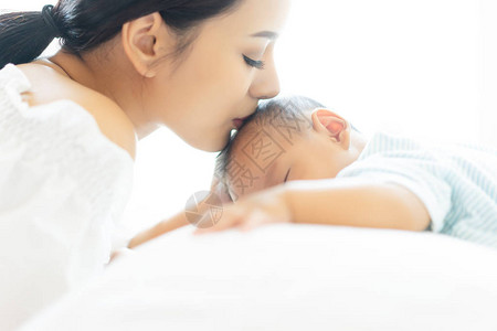 睡觉时把美丽的亚洲年轻女子和她可爱的小儿子关在床上年轻的母亲吻她刚出生的婴儿妈哺乳婴儿产假概念背景图片