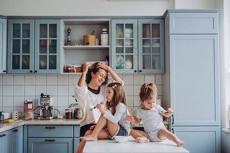 迷人的年轻女人和两个可爱的小女儿在厨房图片