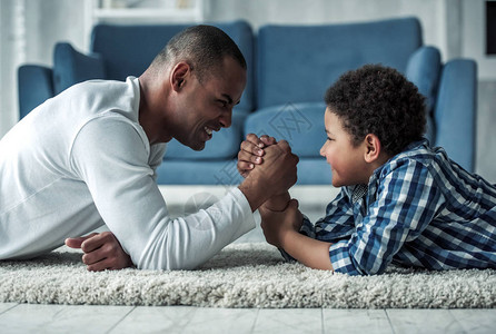 快乐的非裔美国父亲和身着散衣的儿子在家中躺在地毯上时图片