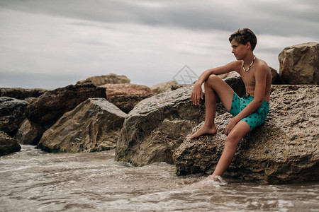 男孩坐在岩石上腿在水中思考图片