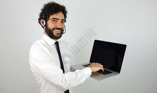 手持笔记本电脑灰色背景的耳机的英俊呼叫中心顾问图片