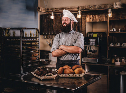 穿着制服的胡子厨师在面包店厨房展示新鲜面包盘图片