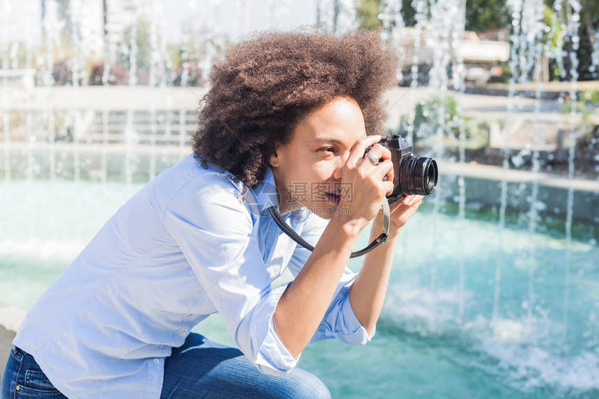 非洲女游客在夏日用旧反光照相机拍摄喷水器照片图片