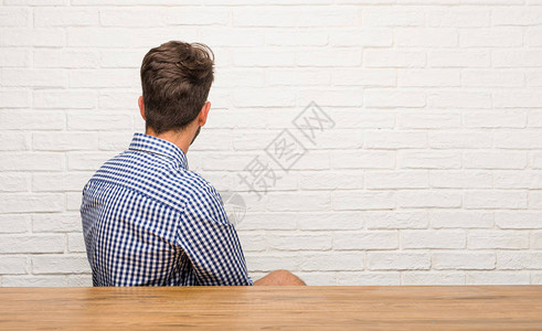 年轻的天主教男子坐着看背摆姿势和等图片