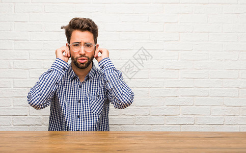 年轻的caucasian年轻男子坐着用双手遮耳朵图片