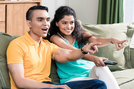 微笑的年轻夫妇一边看电视一边指点图片