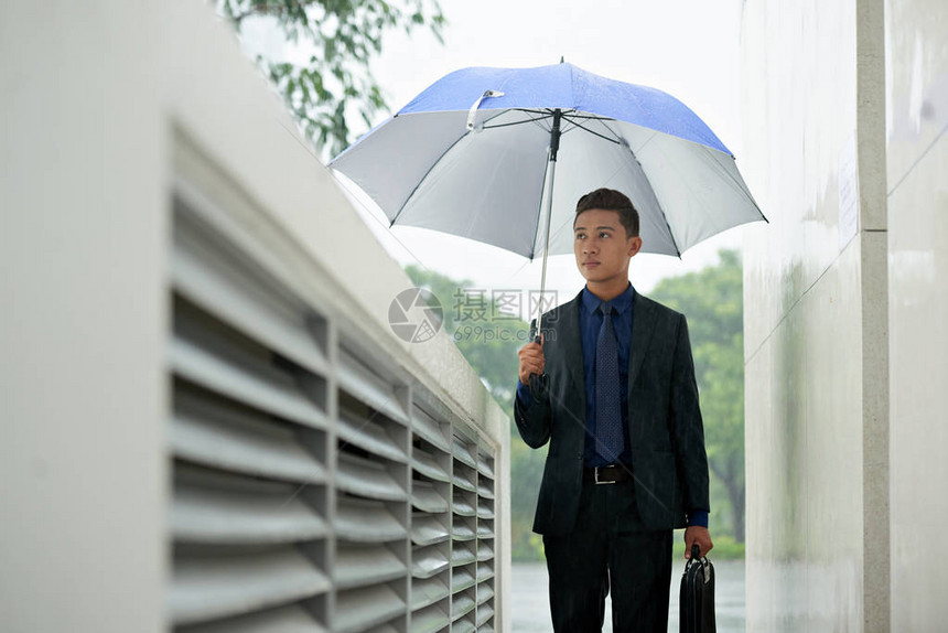 亚洲商人在雨天气下有蓝伞屋图片