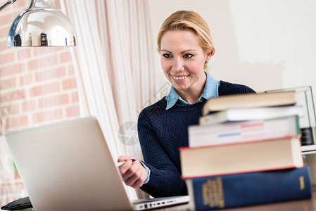 微笑的女人看着笔记本电脑前图片