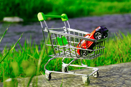 绿草和大自然背景的购物篮中的红玩具车购买汽车时的自然保护概念图片