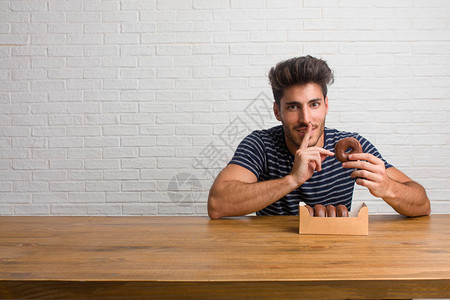年轻英俊自然的男人坐在桌子上保守秘密或要求沉默严肃的脸服从的概念吃图片