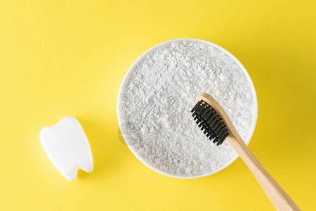 一罐牙齿清洁粉一把木牙刷和一张黄色桌上的假牙背景图片