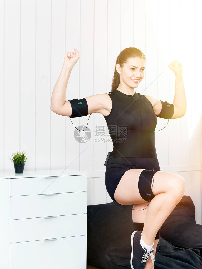 美丽的年轻女孩在机器上锻炼肌肉刺激运动健身的创新技术电动肌肉机图片