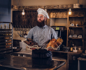 穿着制服的英俊大胡子厨师在面包店厨房展示背景图片