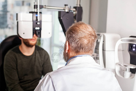 眼科医生在光学商店用光学仪器对年轻人进图片