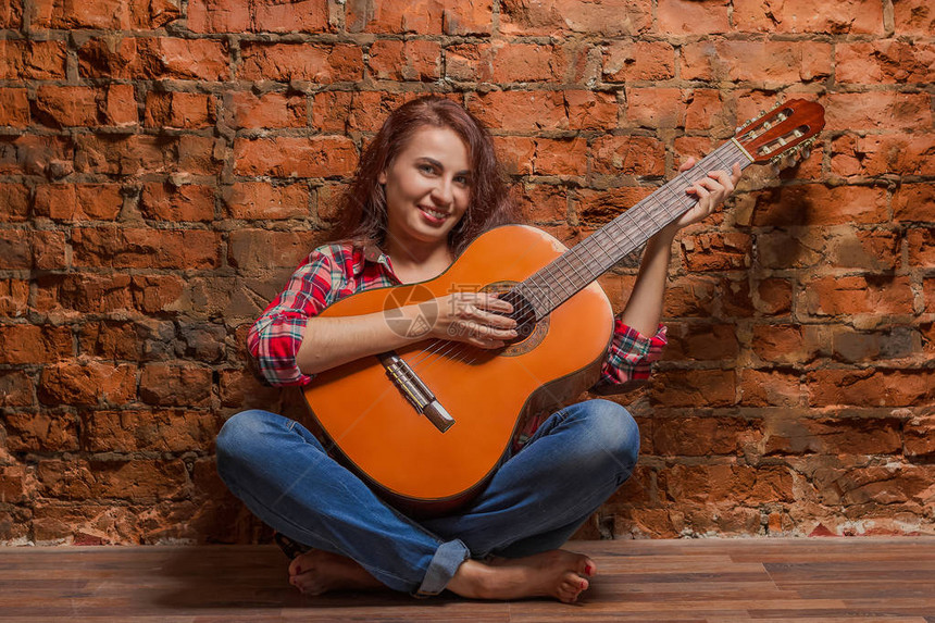 年轻的美少女在红砖墙上弹着akusitcheskuyu吉他音乐图片