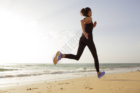 早上在沙滩上跑步的年轻运动女背景图片
