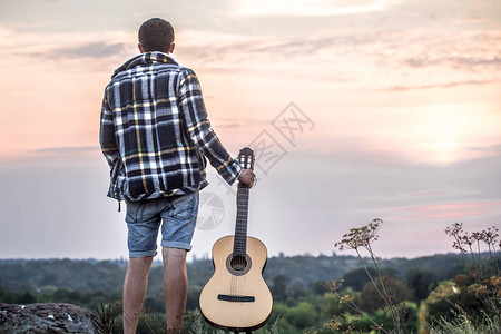 在自然背景和美丽的日落上拿着吉他的人站图片