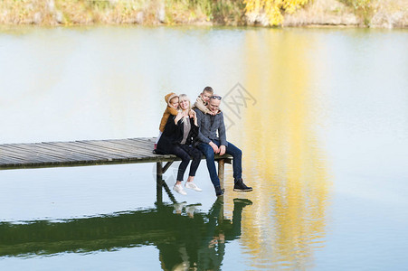 年幼的父母和他们的孩子坐在湖边的码头上图片