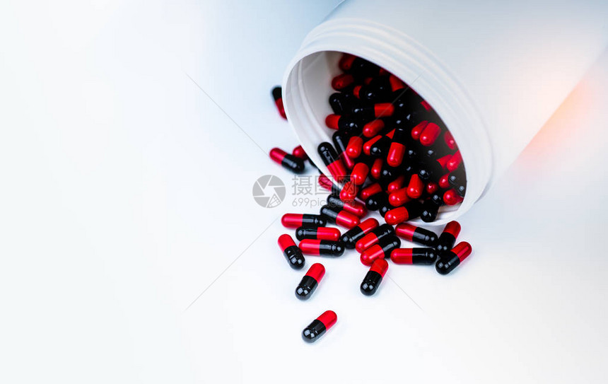 红色黑色胶囊丸从白色塑料瓶容器中溢出抗生素耐药抗菌胶囊丸医药行业药房背景图片