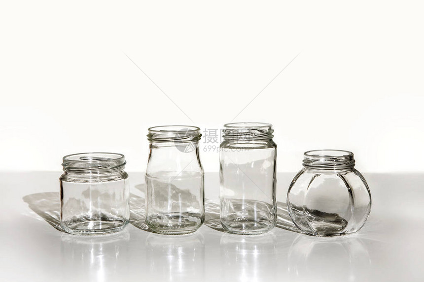 白桌上有四个干净的玻璃罐子和影子在白色背景上隔离图片