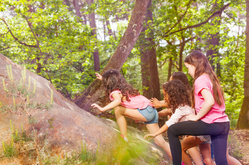 一群小女孩在森林中一个接一个地爬到岩石上图片