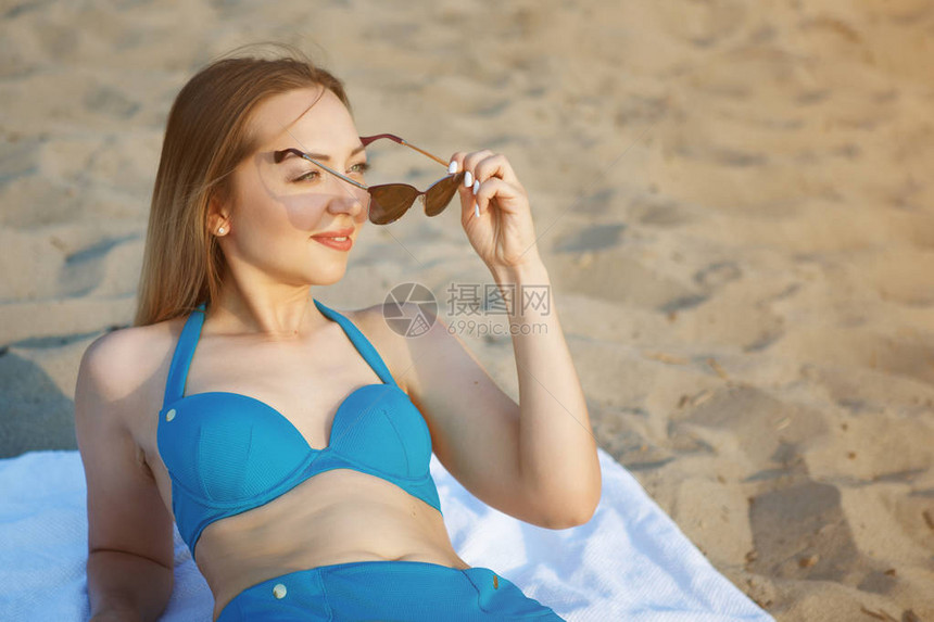穿着蓝色泳衣和太阳镜的年轻美女坐在白图片