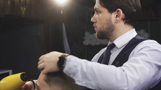 英俊的年轻专业理发师在他的理发店吹干他的客户的头发图片