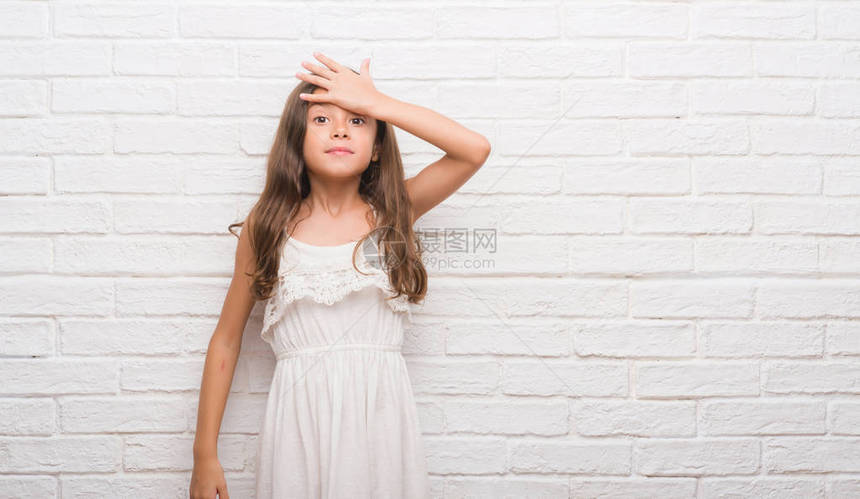 白砖墙旁的年幼西班牙小孩惊讶地用手抓头错误图片