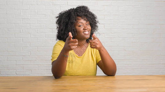 坐在桌上的年轻非洲女用快乐和有趣的面孔对着镜头指手脚图片