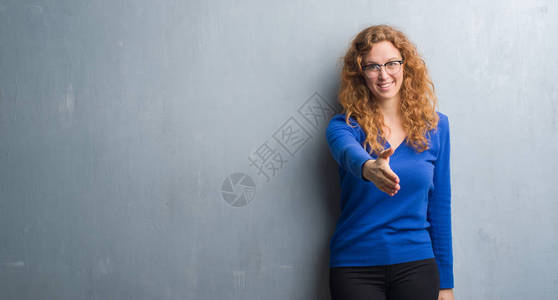 红发女青年在灰色的墙上微笑着亲切的握手作为问候和欢迎成功的业图片