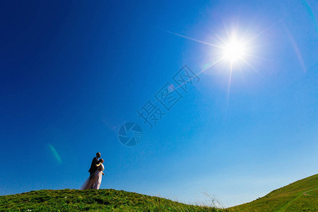 新郎在蓝天和阳光背景下绿草丛生的山顶上图片