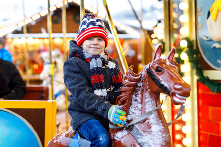 可爱的小男孩骑着一匹快活的旋转木马在圣诞游乐场或市场图片