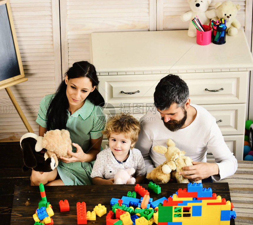 父母和儿子带着笑脸做砖砌建筑妈爸和男孩在木制背景上玩具年轻的家庭花时间在游戏室爱与图片