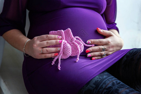 年轻孕妇将粉红色的婴儿袜子放在肚子上图片