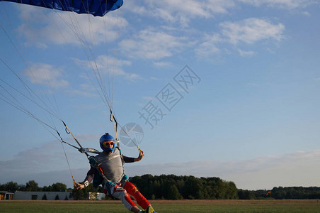 在降落伞的深蓝色小天篷下的跳伞运动员正在降落在机场图片