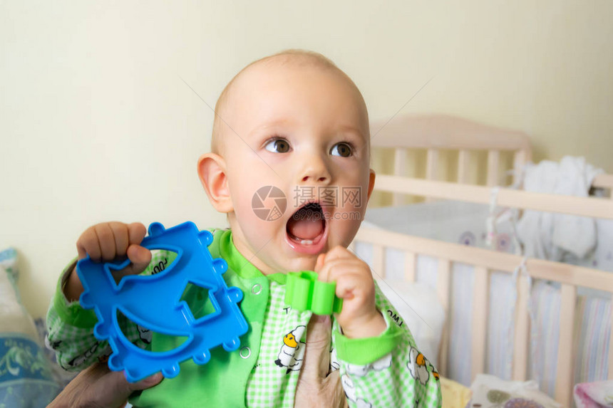一只岁的婴儿因为牙齿长牙而咬着一个塑料玩具带着羊的轻绿色西装图片