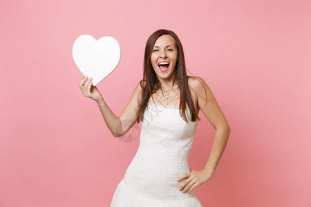 穿着优雅的白色婚纱的兴奋的幸福新娘女人的肖像站在白色的心上图片