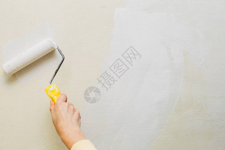 一位女用滚筒和白漆画墙的照片图片