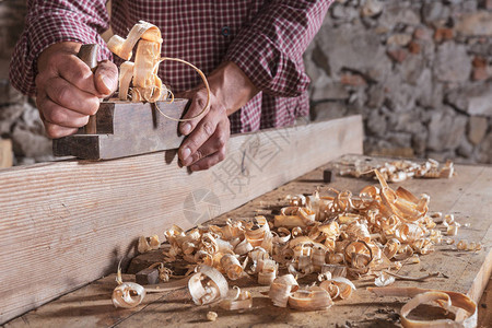 木匠人用手持飞机工具和木板刮碎卷曲木屑图片