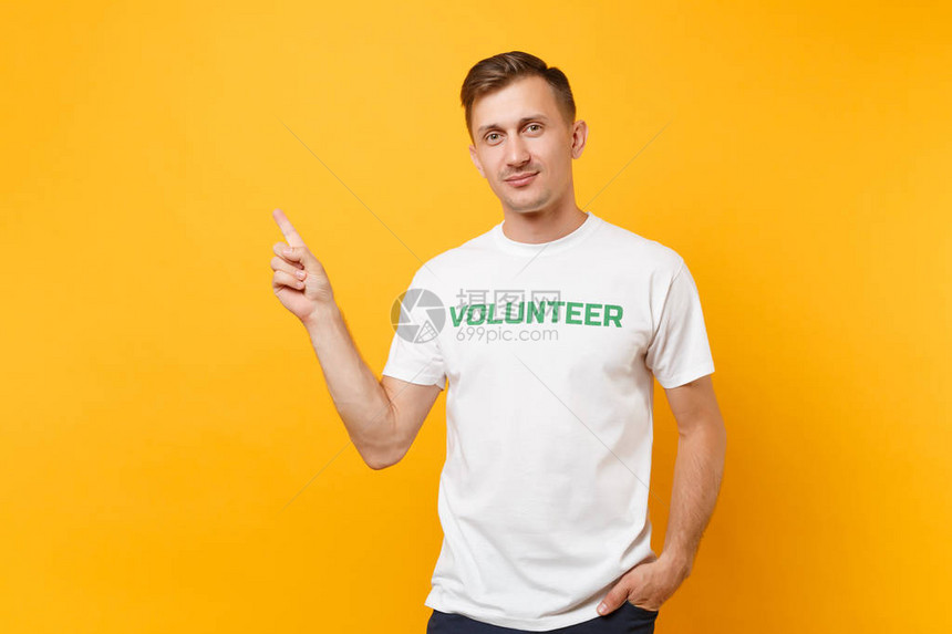 快乐微笑的肖像满意的年轻男子在白色t恤与书面题词绿色标题志愿者孤立在黄色背景自愿无偿帮助图片
