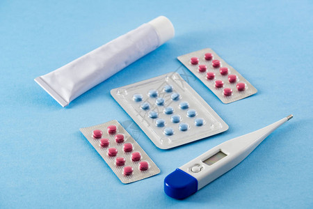 蓝色和粉色药丸白色软膏管和蓝色背景电子数字温度计的泡罩包装图片